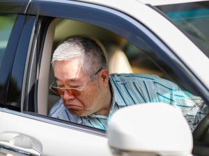 senior man in the front seat of a car looking down at the ground confused