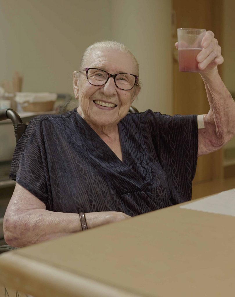 smiling elderly woman raising glass at lynn valley care centre