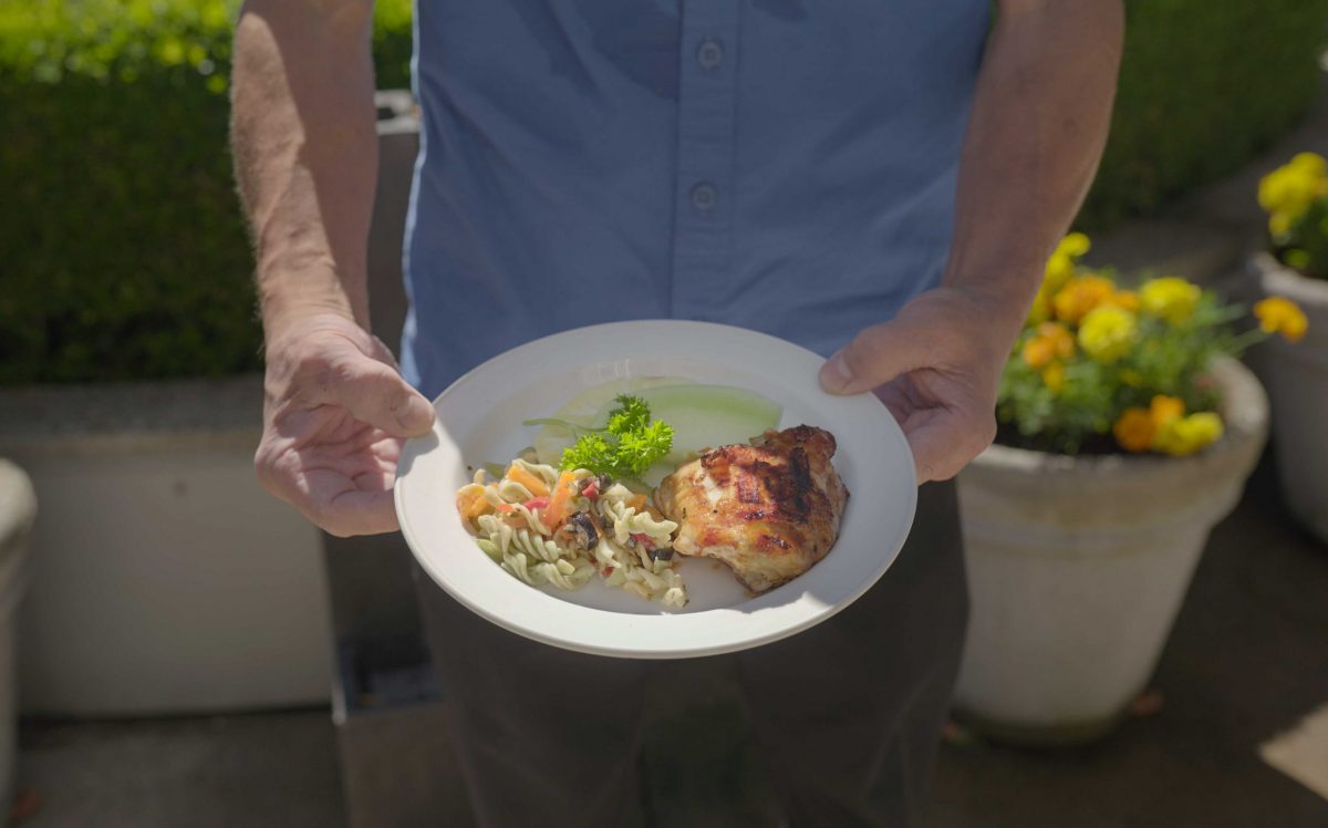 man holding plate of chicken and pasta at lynn valley care centre